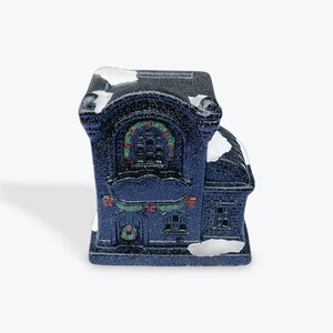 May include: A small, blue ceramic Christmas house with white snow accents. The house has a large window with a wreath and a smaller window with a wreath below it.