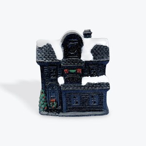 May include: A black and white ceramic Christmas house figurine with a snowy roof, green garland, and a small tree in front.