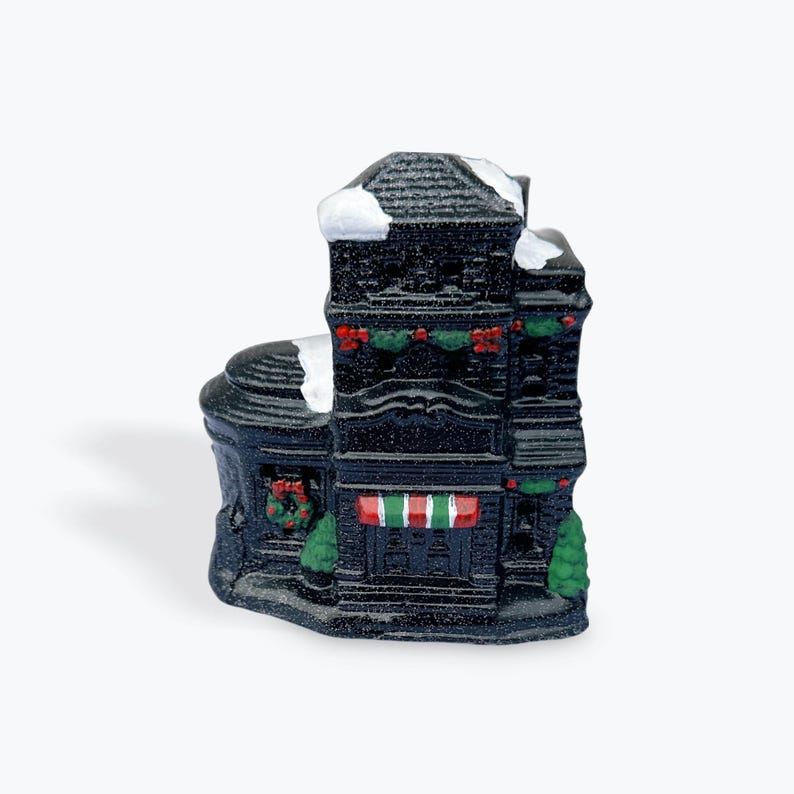 May include: A black and white ceramic Christmas house ornament with a red and white striped awning, green wreaths, and white snow on the roof.
