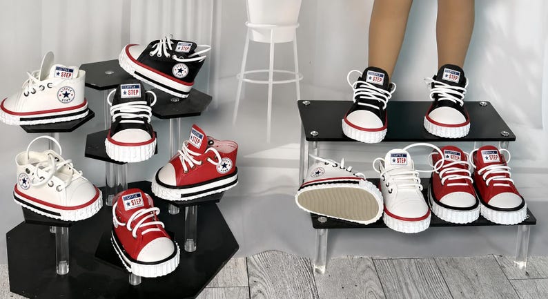 May include: A collection of high-top sneakers in black, white, and red, featuring white laces, white rubber toe caps, and a circular logo on the side with the text Little Step. The shoes are displayed on tiered black acrylic stands.