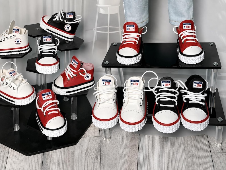 May include: A collection of low-top sneakers in red, black, and white, featuring white laces, white rubber toe caps, and textured white soles. Each tongue displays a rectangular label with the text Little Step and a star icon.