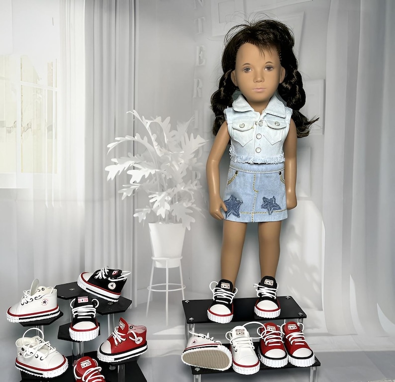 May include: A doll with dark brown hair wearing a light blue denim vest and a matching denim skirt with star appliques. The doll wears black and white sneakers. Several pairs of miniature sneakers in red, white, and black are displayed nearby.