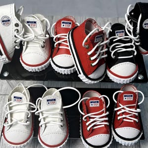 May include: A collection of miniature high-top and low-top sneakers in white, red, and black colors. Each shoe features white laces, a white rubber toe cap, and a circular patch on the side or tongue with the text Little Step and a star icon.