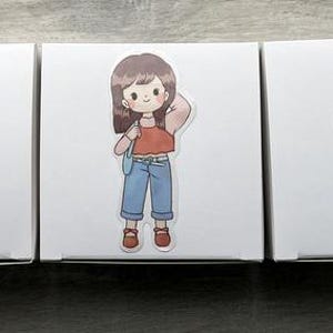 May include: Three white square boxes, each featuring a distinct cartoon sticker. The first shows a person in a yellow jersey with a baseball bat. The second shows a person in a red top and blue jeans. The third shows a person in a blue beret.