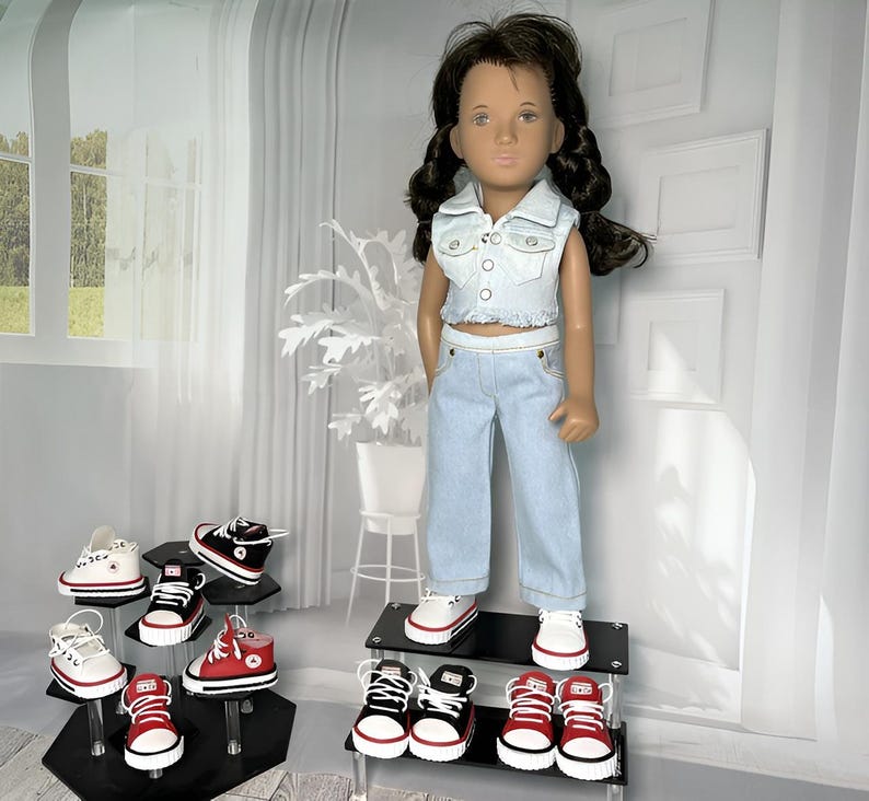 May include: A doll with dark brown hair styled in two braids, wearing a light blue denim vest and matching light blue denim pants. The doll is displayed on a tiered stand alongside several pairs of miniature canvas sneakers in red, black, and white.