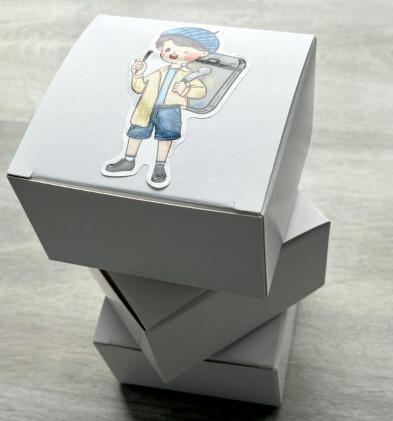 May include: A stack of three plain white square cardboard boxes. The top box features a die-cut sticker of a cartoon character wearing a blue beret, a yellow jacket, and blue shorts, carrying a gray rectangular case and holding a small tool.