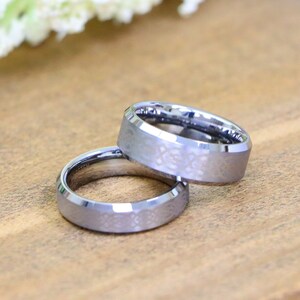 May include: Two silver wedding bands with a brushed finish and beveled edges. The bands are stacked on top of each other.
