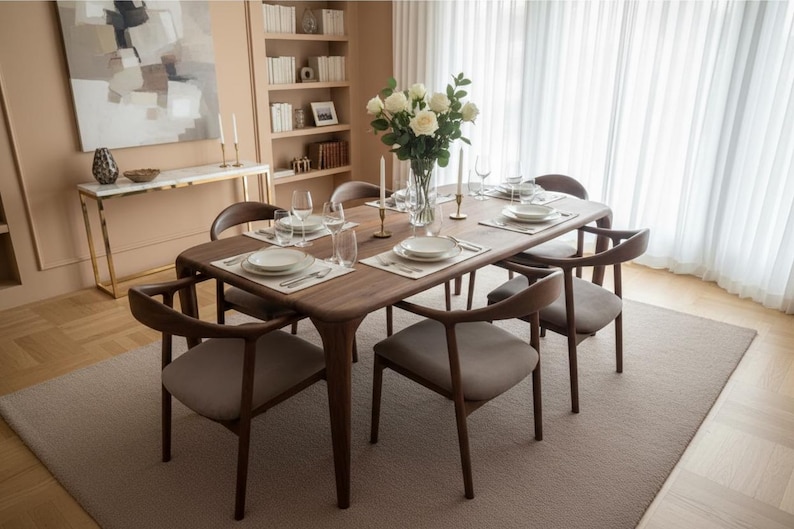 May include: A rectangular wooden dining table with rounded corners and six matching chairs featuring curved backrests and light grey upholstered seats. The table is set with white plates, clear glassware, and a central glass vase of white roses.