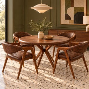 May include: A round wooden dining table with a central pedestal base, accompanied by four armchairs featuring dark brown leather-like upholstery and wooden frames, arranged on a light-colored terrazzo floor in a room with green walls.