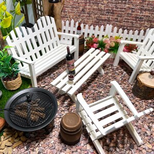 Peut inclure: Ensemble de mobilier de jardin miniature blanc avec un banc, deux chaises, une table et un foyer. L'ensemble est entour&eacute; de petits cailloux et d'une cl&ocirc;ture en bois blanc.