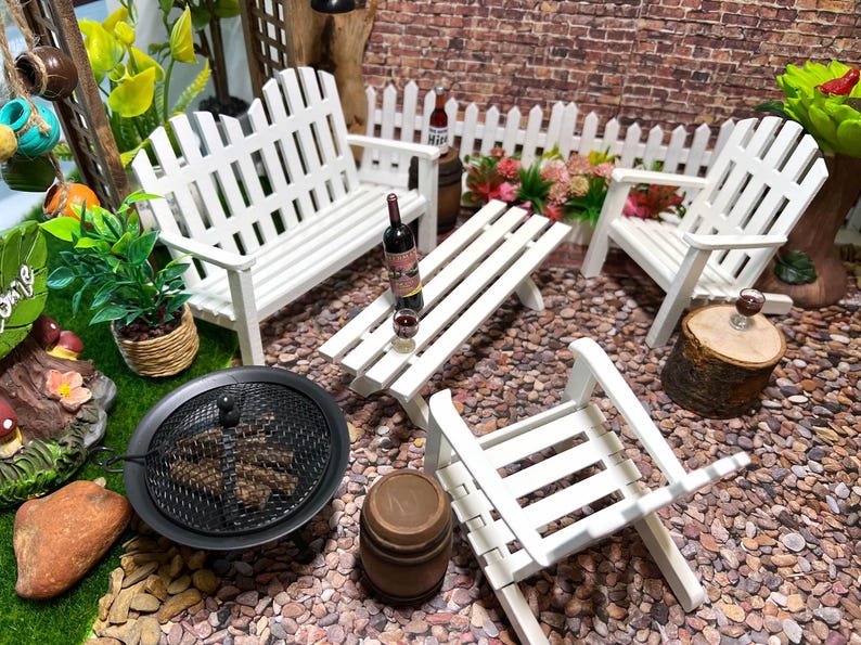 Peut inclure: Ensemble de mobilier de jardin miniature blanc avec un banc, deux chaises, une table et un foyer. L'ensemble est entour&eacute; de petits cailloux et d'une cl&ocirc;ture en bois blanc.