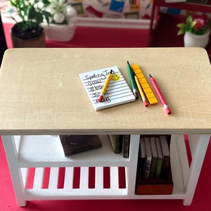 May include: A white wooden table with a light brown top. The table has a shelf with books and a notepad with the words "Spelling Test" written on it. There are pencils and a ruler on the table.
