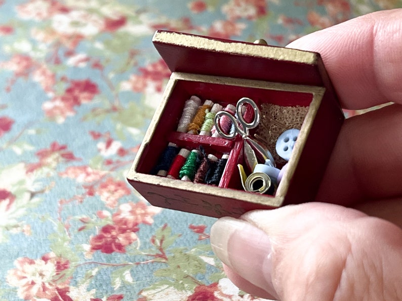 Puede incluir: Una peque&ntilde;a caja de madera roja con tapa abatible, llena de carretes de hilo de colores, un par de tijeras, un rollo de cinta y un bot&oacute;n.