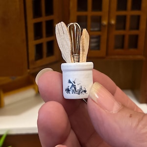 May include: A white ceramic crock with a black and white design of a rooster and chickens. The crock is filled with miniature wooden kitchen utensils, including a whisk, a spatula, and a spoon.