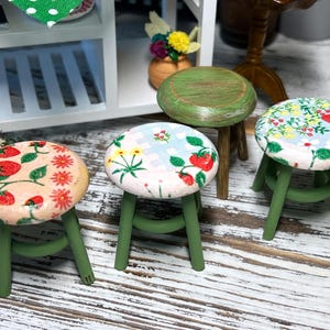 May include: Four miniature green wooden stools with different patterned fabric seats. The seats feature floral designs with strawberries, flowers, and checkered patterns.