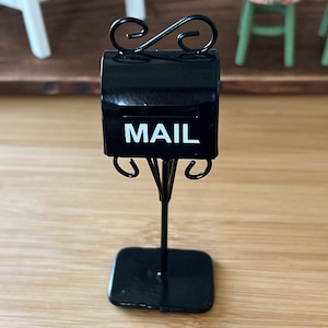 May include: A miniature black metal mailbox with a white "MAIL" sign on the front, mounted on a black metal stand with decorative scrolls.