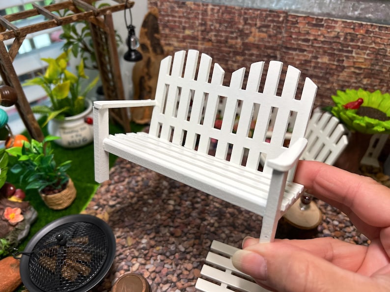 Peut inclure: Banc en bois blanc avec un dossier et un si&egrave;ge de style cl&ocirc;ture &agrave; piquets. Le banc est fait de meubles miniatures pour une maison de poup&eacute;e ou un jardin miniature.