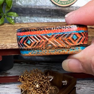 May include: A small terracotta planter with a geometric pattern in shades of orange, brown, blue, and turquoise.