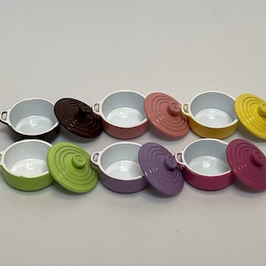 Könnte beinhalten: Satz von acht Miniatur-Töpfen in verschiedenen Farben mit Deckeln. Die Töpfe sind in verschiedenen Farben, darunter Grün, Lila, Rosa, Gelb und Braun. Die Deckel haben ein weißes Innenleben und eine passende Farbe außen.