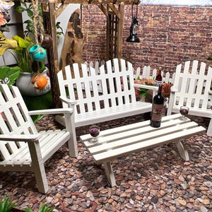 Peut inclure: Ensemble de mobilier de jardin en bois blanc avec un banc, deux chaises et une table basse. Le mobilier est dispos&eacute; sur une surface de gravier. Il y a deux verres de vin rouge sur la table.
