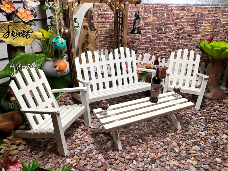 Peut inclure: Ensemble de mobilier de jardin en bois blanc avec un banc, deux chaises et une table basse. Le mobilier est dispos&eacute; sur une surface de gravier. Il y a deux verres de vin rouge sur la table.