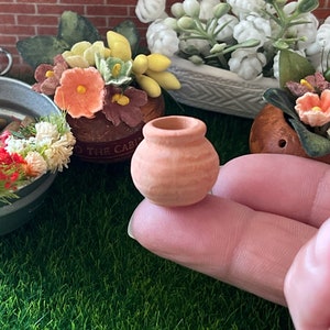 Könnte beinhalten: Ein kleiner Terrakotta-Topf mit runder Form und leicht strukturierter Oberfläche. Der Topf liegt auf einem Finger.