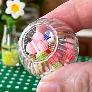 May include: A clear glass jar filled with colourful striped lollipops. The jar is being held by a hand.
