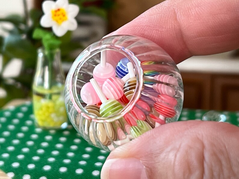 May include: A clear glass jar filled with colourful striped lollipops. The jar is being held by a hand.