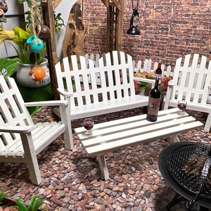 Peut inclure: Ensemble de mobilier de jardin en bois blanc avec un banc, deux chaises et une table. L'ensemble est sur une surface de gravier avec un barbecue noir au premier plan.