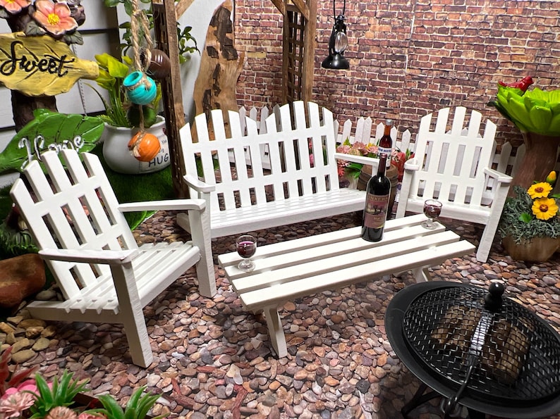 Peut inclure: Ensemble de mobilier de jardin en bois blanc avec un banc, deux chaises et une table. L'ensemble est sur une surface de gravier avec un barbecue noir au premier plan.