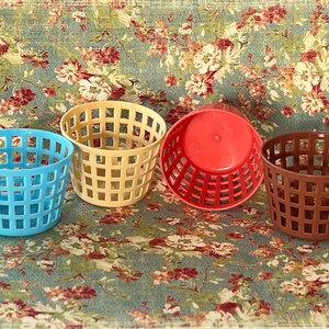 May include: Four plastic baskets in different colors: blue, beige, red, and brown. The baskets have a grid pattern and are ideal for organizing small items.