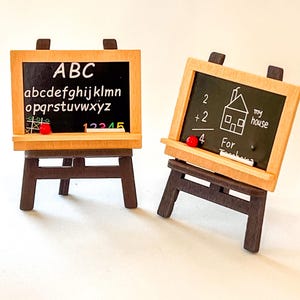 以下が含まれることがあります： イーゼルに置かれた2つのミニチュア木製黒板。1つはアルファベットと数字を表示し、もう1つは簡単な数学の問題と家の絵を表示します。それぞれに小さな赤い磁石と白い消しゴムが付いています。