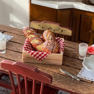 May include: Two pastries, one with a swirl of icing and the other with a cream filling, are displayed in a wooden crate lined with a red and white checkered cloth. The crate is on a wooden table with a glass of milk and a white plate.