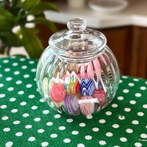 May include: A clear glass jar with a lid filled with colourful candy lollipops. The jar is sitting on a green and white polka dot tablecloth.