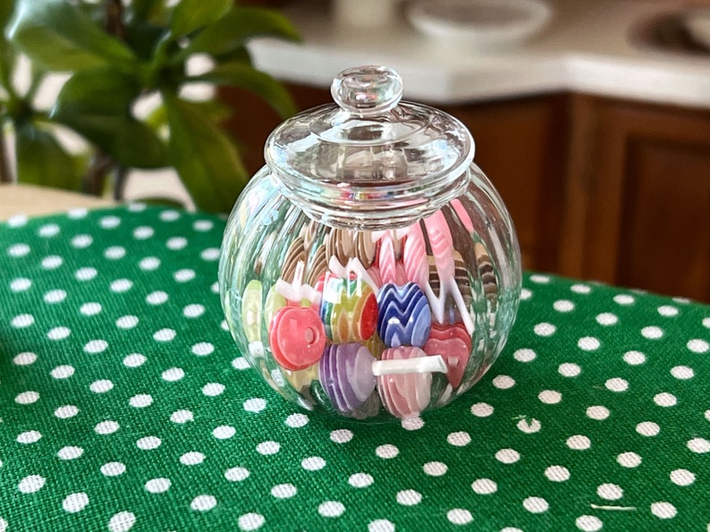 May include: A clear glass jar with a lid filled with colourful candy lollipops. The jar is sitting on a green and white polka dot tablecloth.