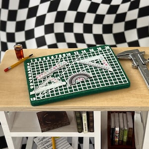 May include: A green cutting mat with a grid pattern and numbers 1-20, a protractor, two rulers, and a silver caliper on a wooden table with a shelf.