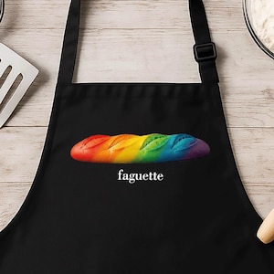 May include: Black apron with two front pockets and a rainbow baguette design. The word "faguette" is printed below the baguette. Baking tools and ingredients, including a whisk, spatula, and flour, are arranged around the apron.