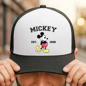 May include: Black and white trucker hat with a white front panel featuring the word "MICKEY" above a cartoon image of Mickey Mouse. The hat includes the text "EST. 1928".