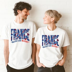 May include: White t-shirts with the word "FRANCE" in blue and red, featuring the Eiffel Tower and stars. The phrase "ALLEZ LES BLEUS!" is printed below the word "FRANCE".