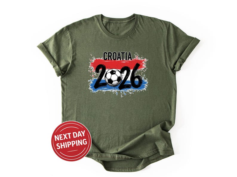 May include: Olive green t-shirt with a graphic featuring the word "CROATIA" above the numbers "26" and a soccer ball. The design incorporates the colors of the Croatian flag: red, white, and blue. A red circle with the text "NEXT DAY SHIPPING" is at the bottom.