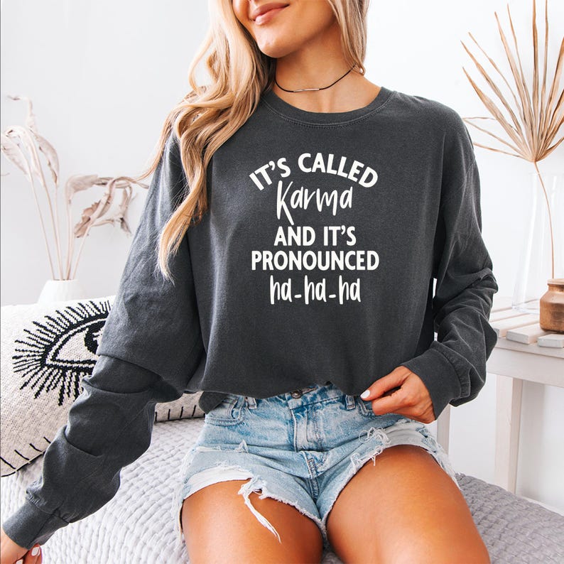 May include: A dark gray cropped sweatshirt with the text "It's called Karma and it's pronounced ha-ha-ha" in white.