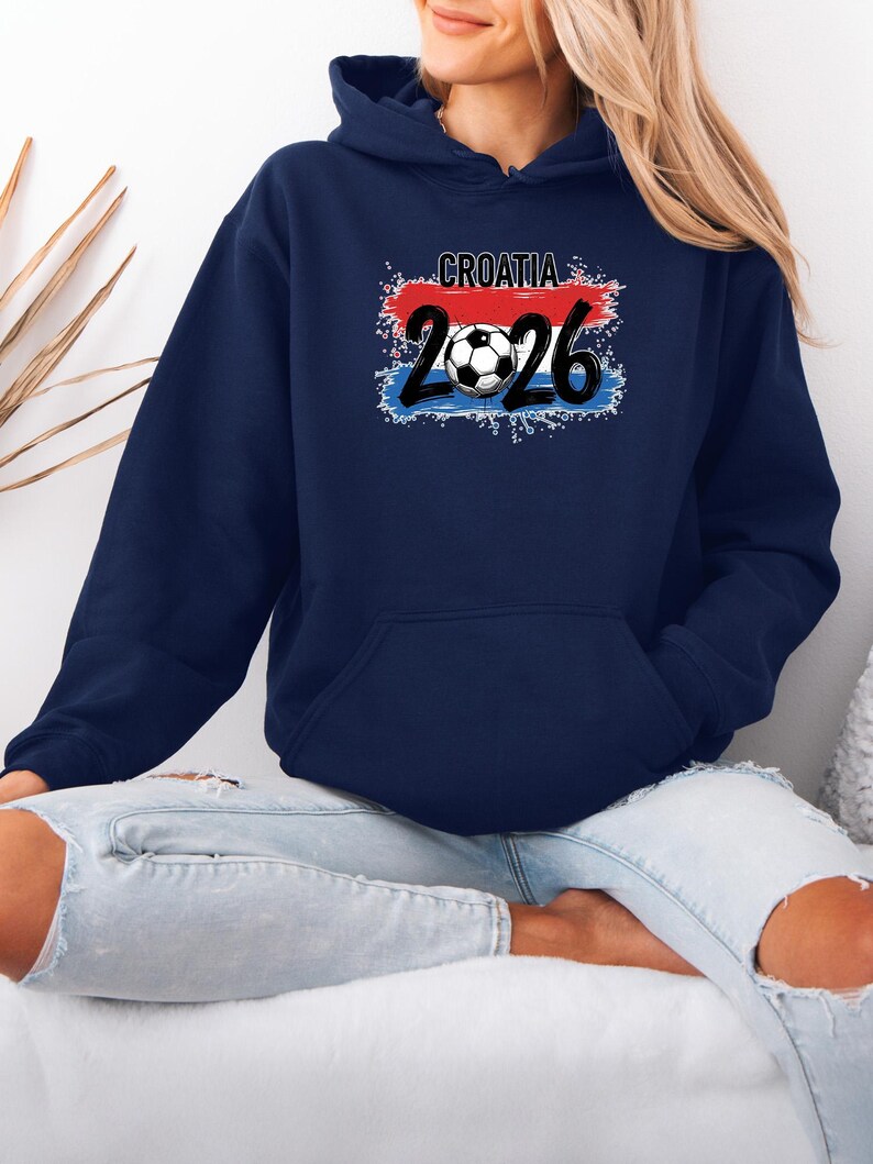 May include: Navy blue hooded sweatshirt featuring the word "CROATIA" above the number "2026" and a soccer ball graphic. The design incorporates the colors of the Croatian flag: red, white, and blue. The sweatshirt has a front pocket and a drawstring hood.