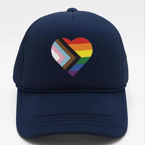 May include: Navy blue trucker hat featuring a heart-shaped design with the Progress Pride flag. The heart includes the colors of the rainbow, transgender flag, and black and brown stripes. The hat has a mesh back.