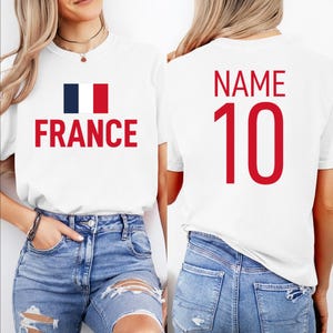 May include: White t-shirt featuring the word "FRANCE" in red, with the French flag. The back of the shirt displays the word "NAME" and the number "10" in red. The shirt is paired with blue denim jeans.