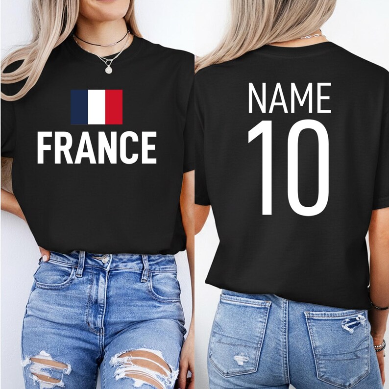 May include: Black t-shirt featuring the word "FRANCE" in white, and the French flag. The back of the shirt displays the word "NAME" above the number "10" in white. The model is wearing blue jeans.