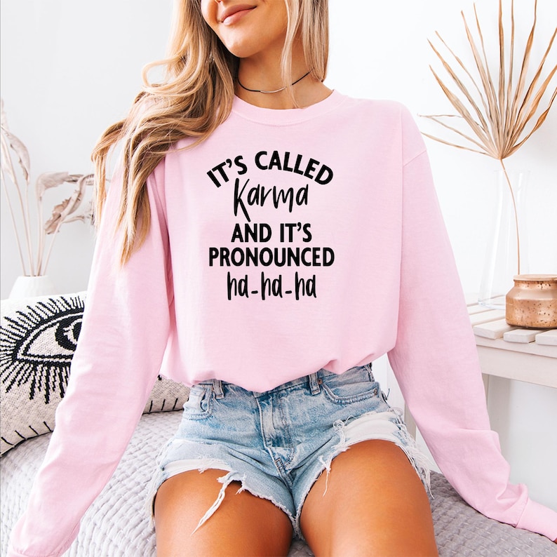 May include: A pink long-sleeved sweatshirt with the text "It's called Karma and it's pronounced ha-ha-ha" printed in black.