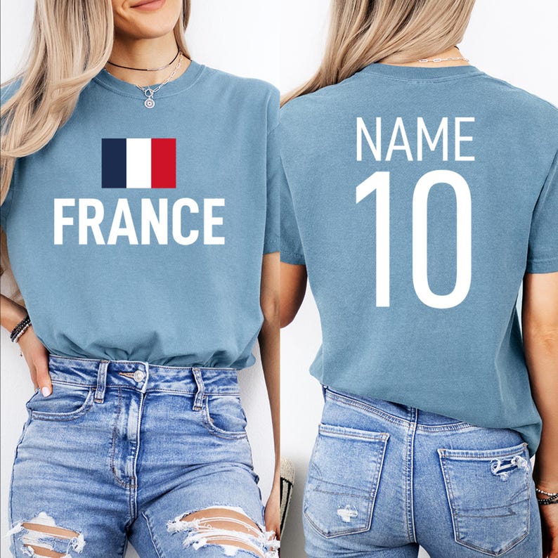 May include: Pale blue t-shirt featuring the word "FRANCE" in white, with the French flag. The back of the shirt displays "NAME" above the number "10" in white. The shirt is made of a soft material.