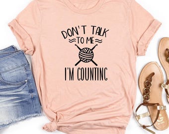 May include: A peach-colored t-shirt with the text "Don't talk to me I'm counting" and a graphic of yarn and knitting needles.