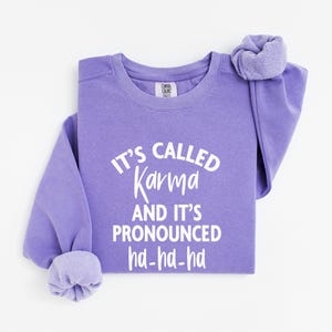 May include: Purple sweatshirt with the text "It's called Karma and it's pronounced ha-ha-ha" in white.