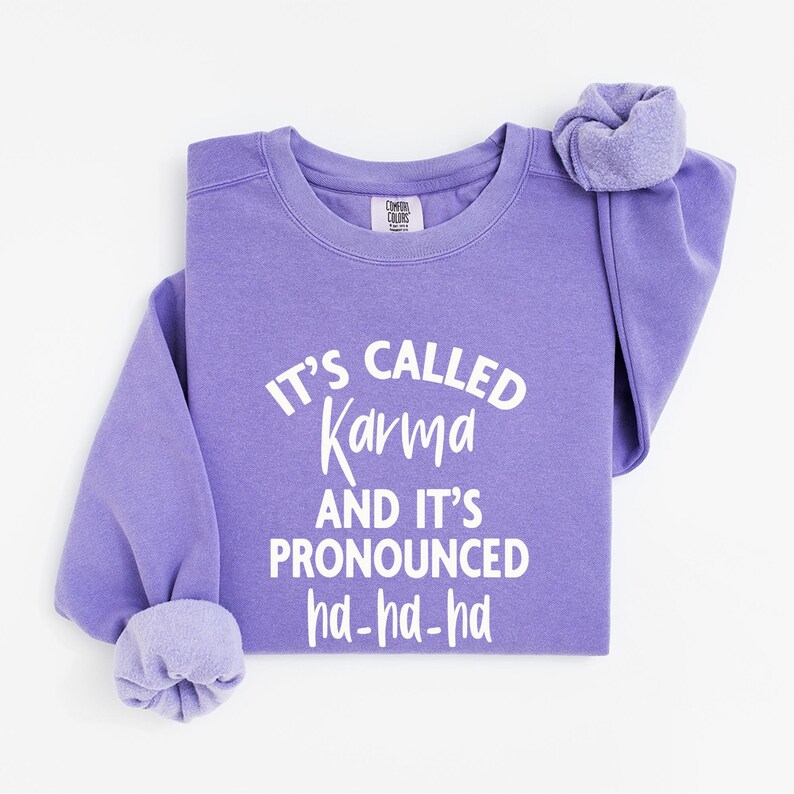 May include: Purple sweatshirt with the text "It's called Karma and it's pronounced ha-ha-ha" in white.